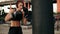 Attractive athletic female boxer in gloves punching a boxing bag. Workout outside. Female boxer training in boxing