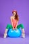 Attractive athletic woman sits on blue fit ball with legs apart