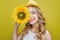 Attractive and awesome young woman is holding a sun flower close to her face. She is looking to camera and smiling. This