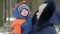 Attractive baby in mother`s arms in the winter. They talk and laugh. Both are dressed in warm blue and orange. The