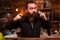 Attractive bartender playing with his long beard behind the counter.