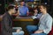 Attractive bartender is smiling and taking order of two men sitting at bar counter in pub