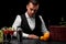 An attractive bartender wipes a bar counter, oranges, lemon, margarita glasses, a shaker on a black background.