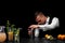 An attractive bartender wipes a shaker, a bar counter with cocktails, limes, lemon and oranges on a black background.