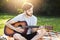 Attractive bearded male guitarist wearing casual clothes sitting crossed legs with guitar liking his hobby while being at green me