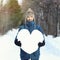 Attractive bearded man holding a huge heart made of snow, standing on snowy road in winter park. Fall in love. Declarations of