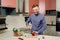 Attractive bearded man with smile cooking festive New Year`s dinner. Man prepares salad of decorated Christmas balls. Concept of