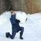 Attractive bearded man standing on knee and holding a huge heart made of snow in his hands, on winter park. Fall in love.