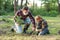 Attractive bearded senior grandfather with his lovely grandson on green lawn planting oak seedling and pour with water.