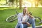 Attractive black man sitting on ground near his bike and speaking on cellphone at park