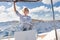 Attractive blond female skipper navigating the fancy catamaran sailboat on sunny summer day on calm blue sea water.