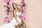 Attractive blonde beauty on a flower swing. Spring concept. Beautiful natural woman in elegant pink dress on a flower swing.