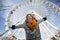 Attractive blonde girl on background of ferris wheel on street. Happy alone weekend