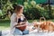 Attractive blonde girl sitting on white blanket in garden with cute welsh corgi puppy in wicker basket and big dog.