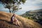 An attractive blonde girl in striped shorts and a blue t-shirt sitting along a path in the hills and ocean