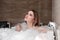 Attractive blonde woman lying in bathtub in foam in hotel.