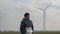 Attractive Blue-Yyed Man With A Beard In A Knitted Hat, Standing In A Field Against The Background Of Windmills