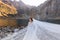 Attractive bride with closed eyes and wavy veil is standing in front of lake surrounded with autumn mountains on the sunny day