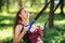 An attractive brown-haired girl with long hair in a tracksuit is doing exercises in the park using a suspension trainer