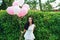 Attractive brunette with balloons near the green hedgerow