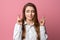 Attractive brunette girl cross fingers good luck, praying for wish come true. Studio shot, pink background