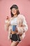 Attractive brunette girl in faux pink fur holding popcorn in hand. Wearing in black shorts white top black cap and