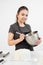 Attractive brunette girl pastry chef in apron whips cream cake in a metal bowl.