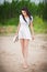 Attractive brunette girl with short white dress strolling barefoot on the countryside road. Young beautiful woman walking