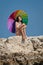 Attractive brunette with iridescent umbrella on wild rocky beach