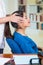 Attractive brunette office woman wearing blue sweater sitting by desk receiving head massage, stress relief concept