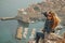 Attractive brunette seen from behind posing while sitting on a stone above the city of Dubrovnik, outlines of the majestic old