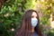 Attractive brunette wearing a light blue surgical mask looking into the distance with a worried unsure look on her face. Sunlight