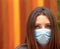 Attractive brunette wearing a surgical face mask looking confidently straight at the camera. Closeup with her amber eyes matching