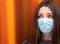 Attractive brunette wearing a surgical face mask with a surprised optimistic expression. Closeup with her amber eyes matching the