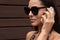 Attractive brunette woman in dark sunglasses has phone conversation on mobile phone outdoors, looking at distance, looks calm,