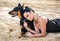 Attractive brunette woman with a doberman lying on the sand