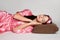 Attractive brunette woman in pink gown is laying on pillow with eyes closed on floor with blindfold