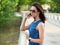 Attractive brunette woman in sunglasses and blue jeans dress has emotional phone conversation on mobile phone on park bridge outdo