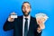 Attractive business man with long hair and beard holding credit card and euros making fish face with mouth and squinting eyes,