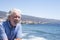 Attractive and carefree senior man with beard and white hair  leaning against the railing of the seafront in a sunny day - wind,