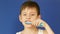 An attractive caucasian boy of 8 years old brushes his teeth and sings looks at the camera on a blue background, studio shooting.
