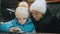 Attractive caucasian mother and daughter using smartphone sitting in cafe. Advanced little child shows and explains to