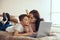 Attractive Caucasian mother kissing small teen son lying on bed, looking at laptop screen.