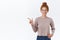 Attractive, charismatic redhead woman with curly hair combed in messy bun, hold hand in pocket, pointing left, introduce