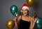 Attractive charming Hispanic woman with perfect toothy smile wearing Santa hat, holds Christmas gift in shiny green wrapping paper