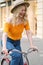 Attractive cheerful blond girl in hat joyfully riding on classic bicycle through street