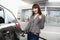 Attractive cheerful young business woman, smiling and showing her thumb up to camera, while refueling her luxury car at
