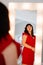 an attractive chubby woman in a red dress looks in the mirror.