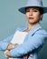 Attractive confident short haired brunette woman in blue business smart casual suit and hat standing looking at camera