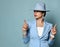 Attractive confident short haired brunette woman in blue business smart casual suit and hat standing pointing up with